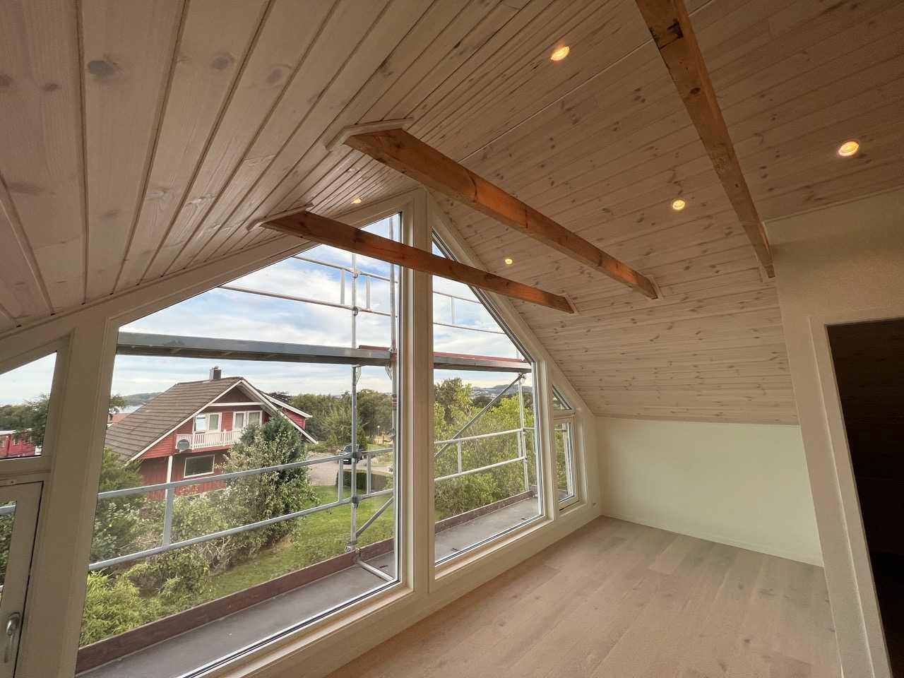 Loft med nytt panel i taket, synlige bjelker og store vinduer